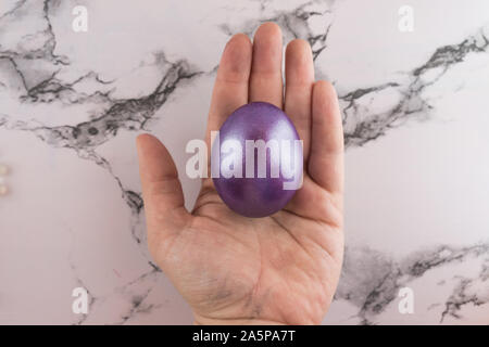 Marble Easter flat lay background with painted Easter egg in female hand. Stock Photo