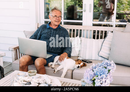 Man using laptop, sitting next to dog on sofa Stock Photo