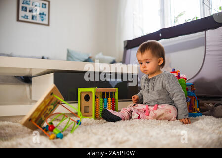 Cute little baby playing with toys in living room on a carpet floor. Stock Photo