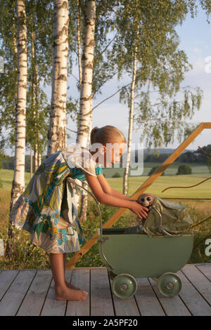 Girl putting stuffed monkey into baby carriage Stock Photo