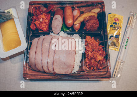 Jeju Island, South Korea, september 06, 2019: close up view of open korean lunchbox with spam, sausages, kimchi and marinated daikon as side dish Stock Photo