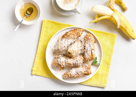 Tasty dessert from pan fried bananas in asian style. Deep fried bananas on plate over white stone background. Top view,flat lay Stock Photo