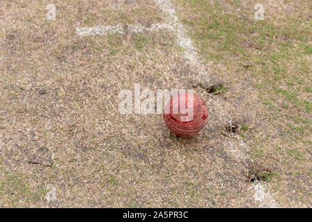 A close up view of a old well used red cricket ball on a grass pitch Stock Photo