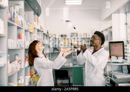 Two funny smiling young pharmacists having fun in pharmacy, throw up different pills Stock Photo