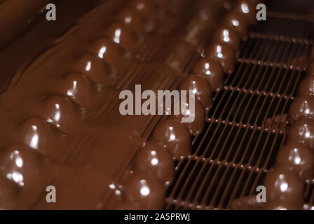 chocolates just poured with liquid chocolate on a conveyor belt of a confectionery factory close-up Stock Photo
