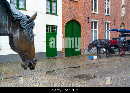Horse-drawn carriage with tourists and Drinking fountain for horses in historic center of Bruges, Belgium, selective focus. Stock Photo
