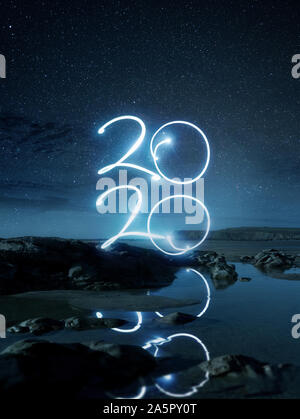 Happy New Year2020 light effect writing reflecting in water on a beach at night. Long exposure Landscape photo composite. Stock Photo