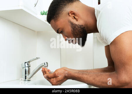 Black guy washing face in bathroom, side view Stock Photo