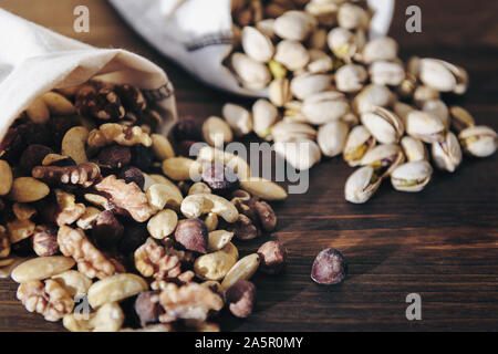 mixed nuts, pistachios and dry fruits in burlap bags on wooden table, healthy food and snack concept Stock Photo