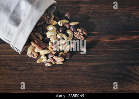 mix of nuts and dry fruits in burlap bag on wooden background, healthy food and snack concept, copy space for text Stock Photo
