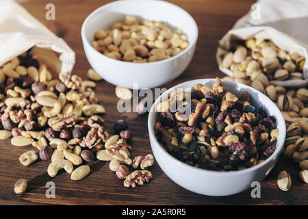 selection of mixed nuts and dried fruit in white bowls and burlap sack on a wooden table, healthy food and snack concept Stock Photo