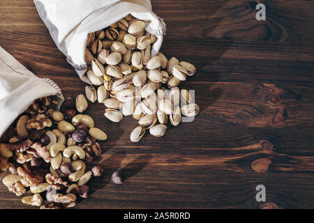 mix nuts, dry fruits and pistachios on a wooden background in hessian bags, healthy food and snack concept, copy space for text Stock Photo