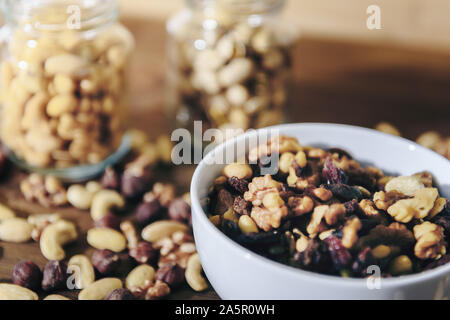 white bowl with varied organic dried fruits and glass jars with mixed nuts in the background on rustic wooden table, healthy food and snack concept, c Stock Photo