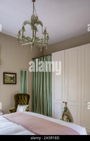 Bamboo chandelier above bed with green door curtain and built-in wardrobe Stock Photo