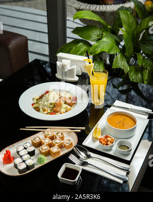 lunch setup with lentil soup, caesar salad, sushi set and orange juice Stock Photo