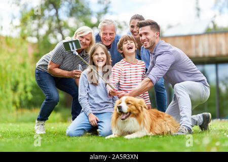Three Generation Family Taking a Selfie in the Garden with Dog with Selfie Stick Stock Photo
