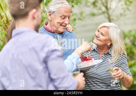 Happy seniors couple celebrates birthday with pie and candles in the garden Stock Photo