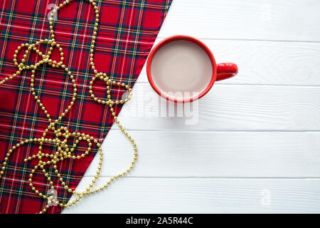 Scottish fabric, a red cup of hot cacao on white wooden table. Golden Christmas beads decorations. Copy space, space for text. Stock Photo