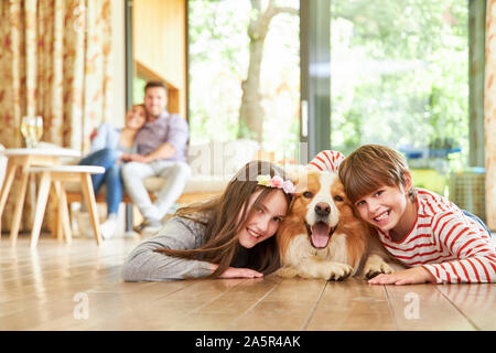 Two cheerful children cuddle with their dog on the living room parquet Stock Photo