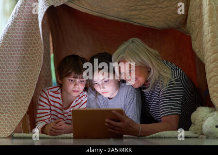 Kids and grandma using tablet computer while surfing the internet under blanket as a tent Stock Photo