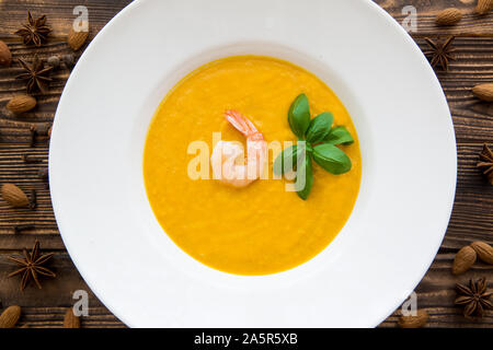 Tasty pumpkin cream soup with shrimps and basil leaves, blended with spice and carrots. Top view. Stock Photo