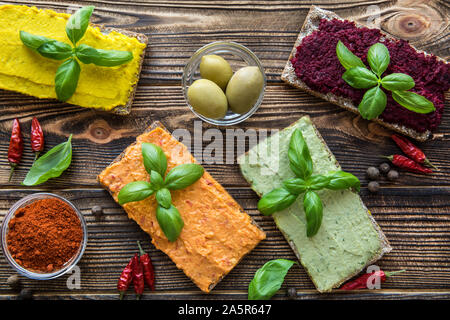 Different kinds of hummus on brown table. Sweet paprika, curry spice taste, beetroot with frsh asil eaves and avocado. Stock Photo