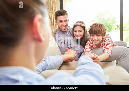 Children and father play and run with their mother on the couch at home Stock Photo