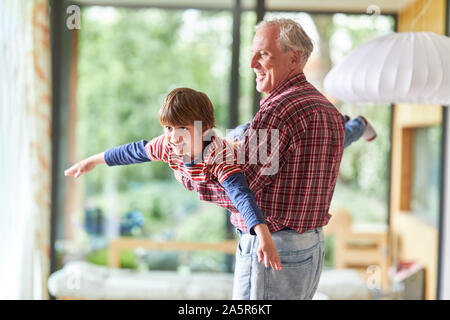 Grandfather makes happy grandson fly at home in the living room Stock Photo