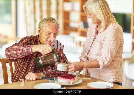 Senior couple having coffee together with cake in living room Stock Photo