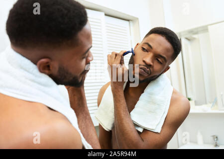 Black millennial guy shaving his beard in bathroom Stock Photo