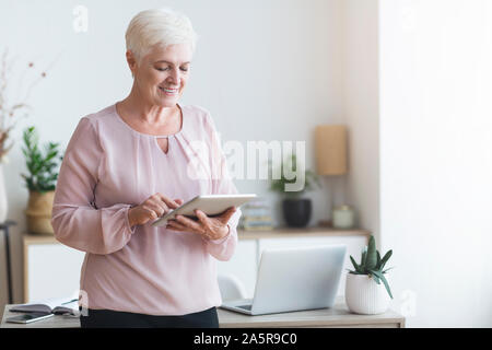 Smiling beautiful senior woman using digital tablet Stock Photo