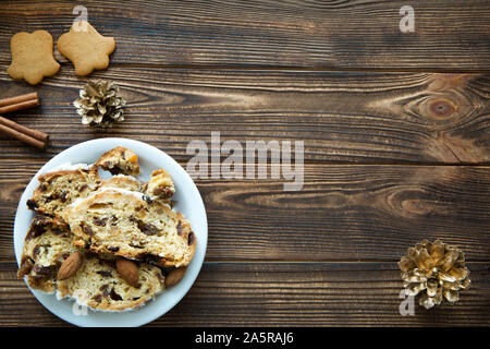 Christmas cake and gingerbread cookies on brown wooden table. Golden cones and cinnamon sticks decorations. Free space for text. Space for greeting an Stock Photo
