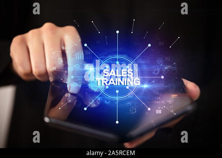 Businessman holding a foldable smartphone with SALES TRAINING inscription, new business concept