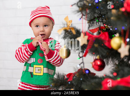 CAdorable baby elf eating lollipop near Xmas tree Stock Photo