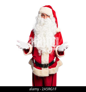 Middle age handsome man wearing Santa Claus costume and beard standing smiling cheerful with open arms as friendly welcome, positive and confident gre Stock Photo