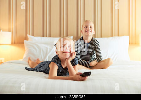 Smiling little girl and her cute brother watching television togeter while relaxing on a bed Stock Photo