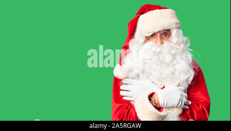 Middle age handsome man wearing Santa Claus costume and beard standing shaking and freezing for winter cold with sad and shock expression on face Stock Photo