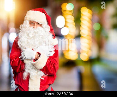 Middle age handsome man wearing Santa Claus costume and beard standing shaking and freezing for winter cold with sad and shock expression on face Stock Photo