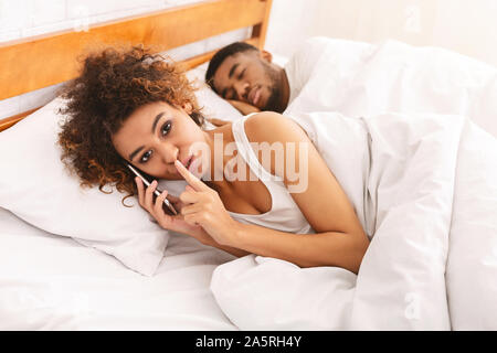 Black wife cheater talking privately on cellphone in family bed Stock Photo