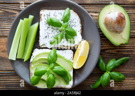 A plate of healthy snack. Avocado sandwiches with celery sticks, goat cheese, quinoa and a slice of lemon. Top view. Stock Photo