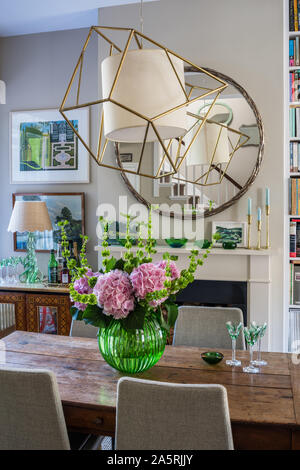 Large metal framed pendant reflected in mirror above dining table. Stock Photo