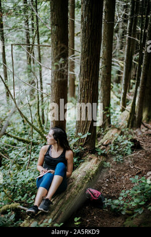 A woman writes in a journal while hiking in a forest in Washington Stock Photo