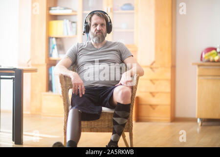 older man with prosthetic leg hearing music in a chair Stock Photo