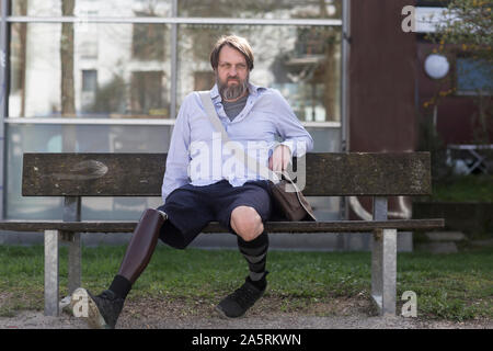 older man with prosthetic leg sitting on a bench Stock Photo