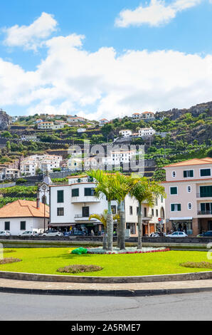 Ribeira Brava, Madeira, Portugal - Sep 9, 2019: City center on a vertical picture with palm trees. Buildings on the hills in the background. Green trees and banana plantations among the houses. Stock Photo
