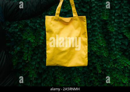 Handmade shopping bag on green plant background. Blank canvas bag. Mockup for design Stock Photo