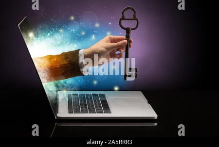 Hand with huge vintage key coming out of a laptop with sparkling effects Stock Photo