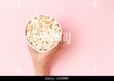 Unhealthy diet concept. Food composition of hand holding popcorn in bucket on pink background top view copy space Stock Photo