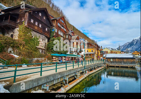 HALLSTATT, AUSTRIA - FEBRUARY 21, 2019: Embankment of Hallstattersee boasts extant historical houses, small tourist market with souvenirs, authentic b Stock Photo