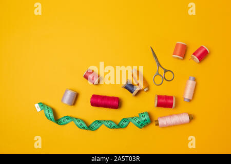 Multi-colored threads pink reels, measuring tape, sewing machine needles on a background. Sewing accessories for needlework, sewing. Stock Photo
